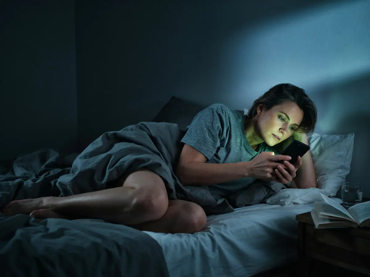 Jemand liegt um 2 Uhr nachts wach im Bett, nur vom Handy beleuchtet